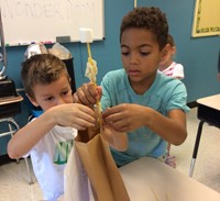 Two students work together in the Wonder Room to try and build the tallest structure using dry spaghetti, marshmallows, tap, and a brown bag