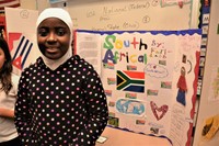 A student stands in front of the South Africa tri-fold board she created