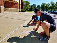Gavin and Henry Farkasovsky contribute to the positive messages and artwork drawn in chalk at the entrance of Alcott Elementary School.